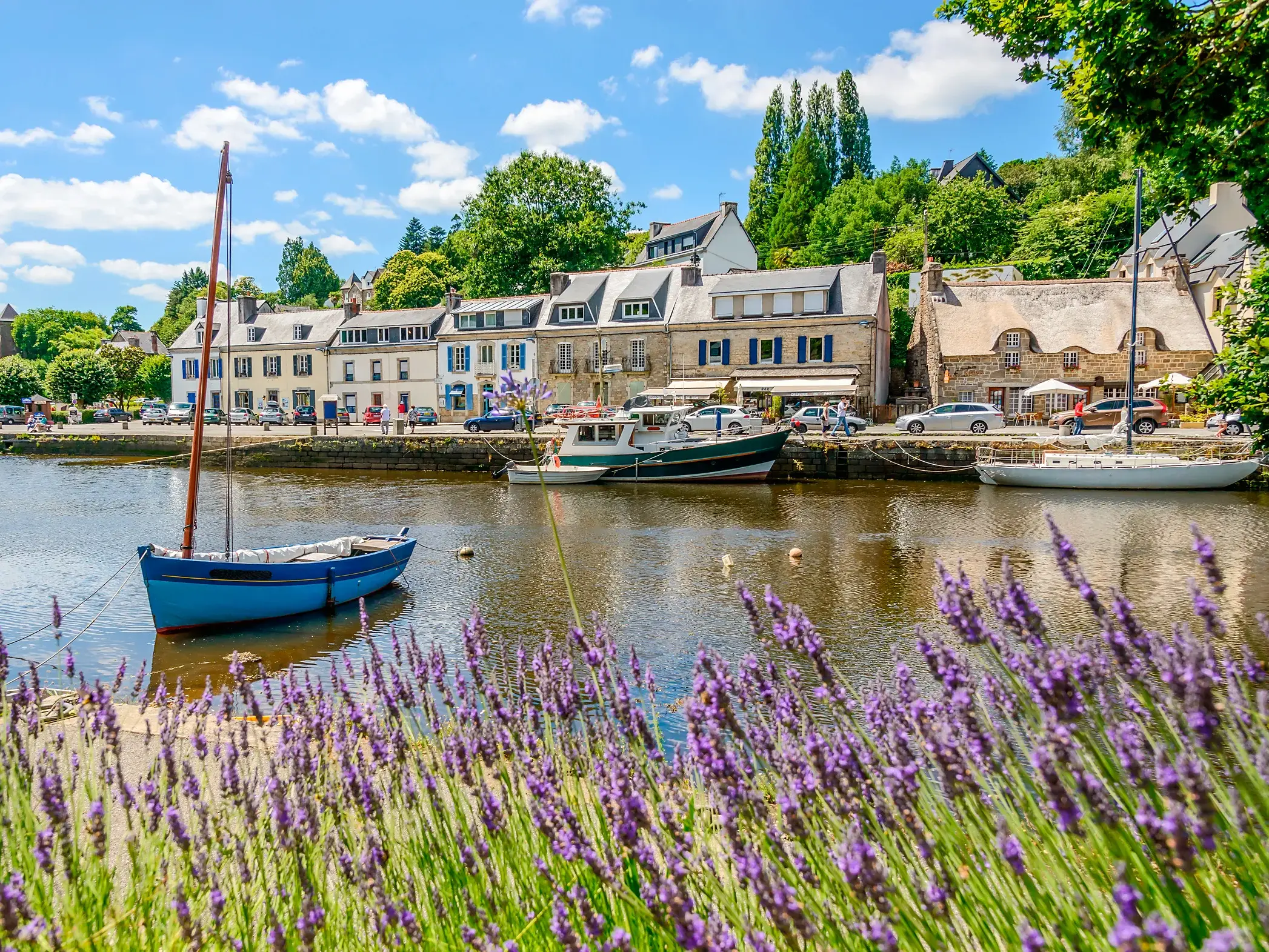 Malerischer Hafen von Pont-Aven in der Bretagne mit Booten, historischen Häusern und blühendem Lavendel am Flussufer.