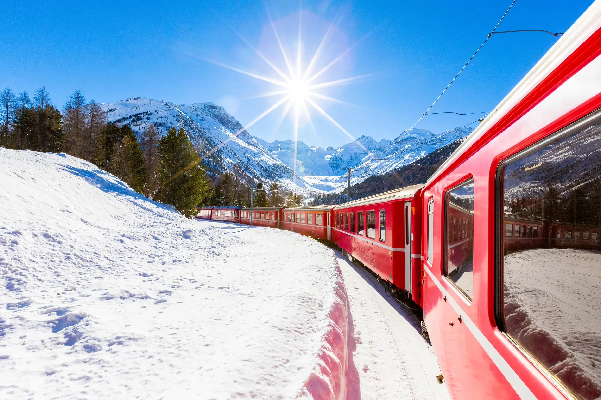 Bernina Express fährt bei strahlendem Sonnenschein durch die verschneite Schweizer Alpenlandschaft