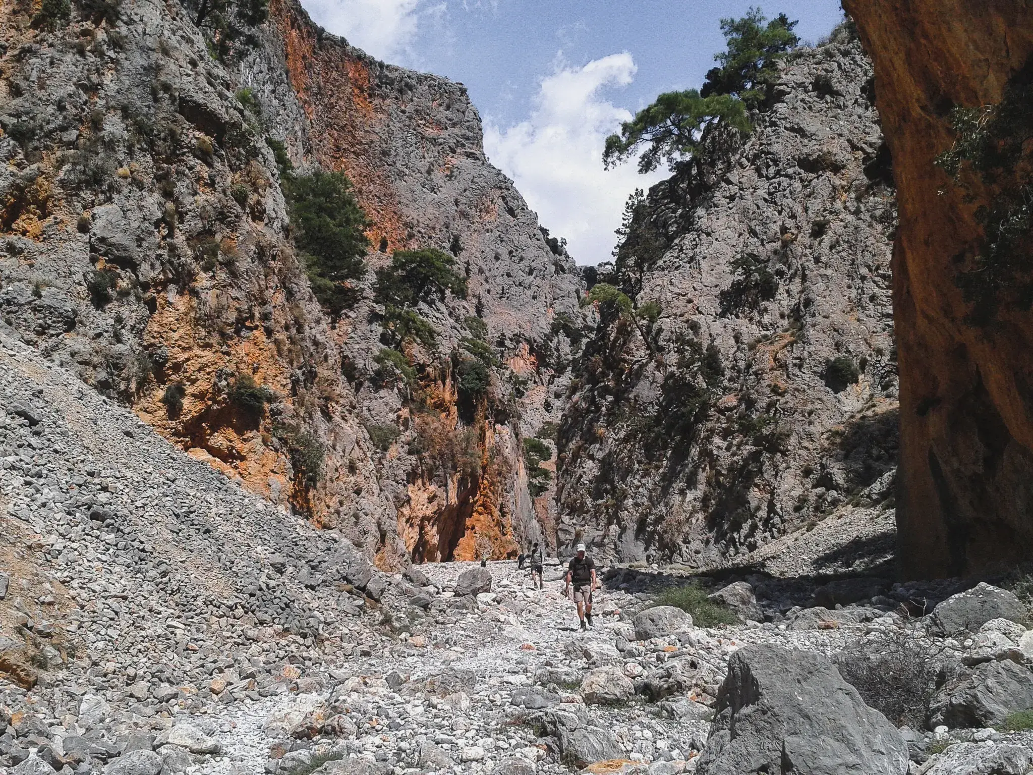 Ein Wanderer durchquert auf einem steinigen Pfad die gewaltige Samaria-Schlucht auf Kreta, flankiert von steilen Felswänden.