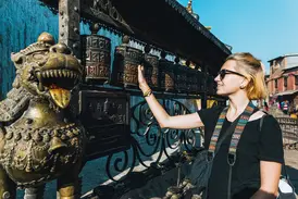 Junge Reisende dreht lächelnd eine Gebetsmühle am Pilgerweg Barkhor in Lhasa, Tibet, neben einer bronzenen Löwenstatue.