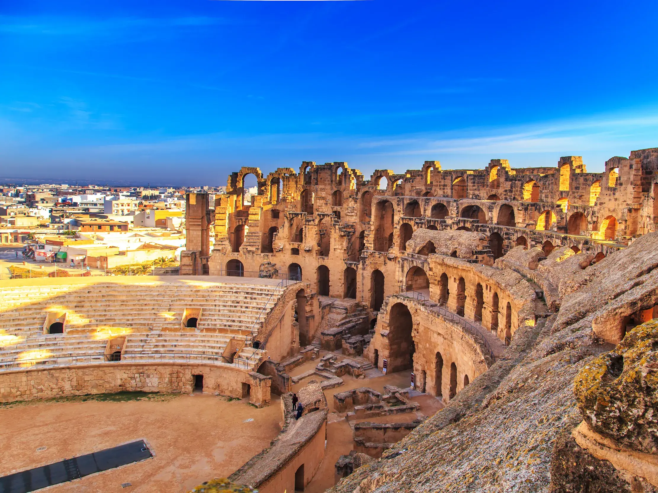 Blick von den Rängen auf die sandige Arena des imposanten römischen Amphitheaters in El-Djem bei strahlend blauem Himmel.