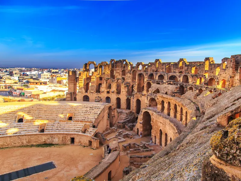 Blick von den Rängen auf die sandige Arena des imposanten römischen Amphitheaters in El-Djem bei strahlend blauem Himmel.