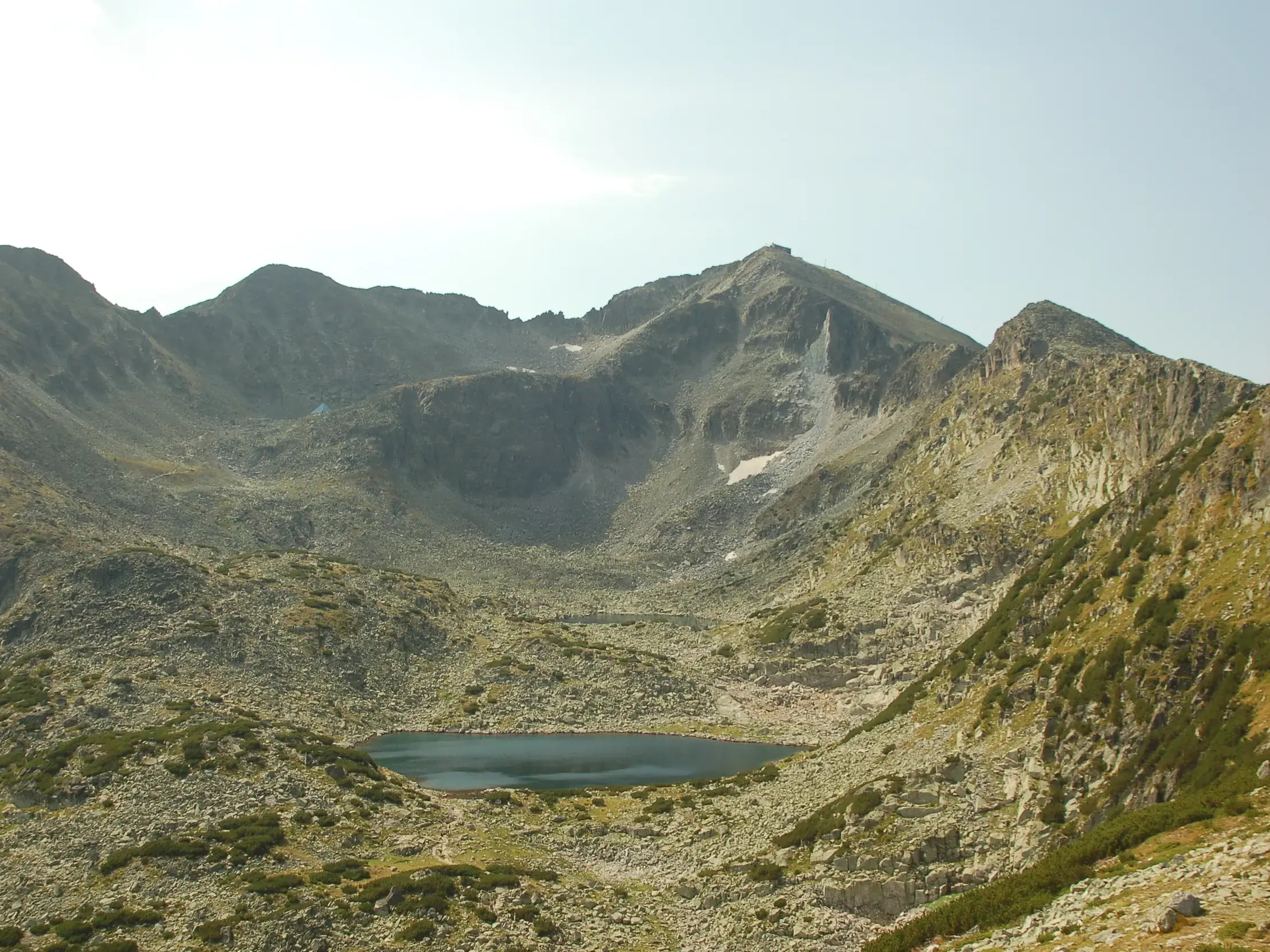 Tiefblauer, glasklarer Bergsee, eingebettet in einem weiten, felsigen Kar der schroffen Gipfel des Rila-Gebirges in Bulgarien.