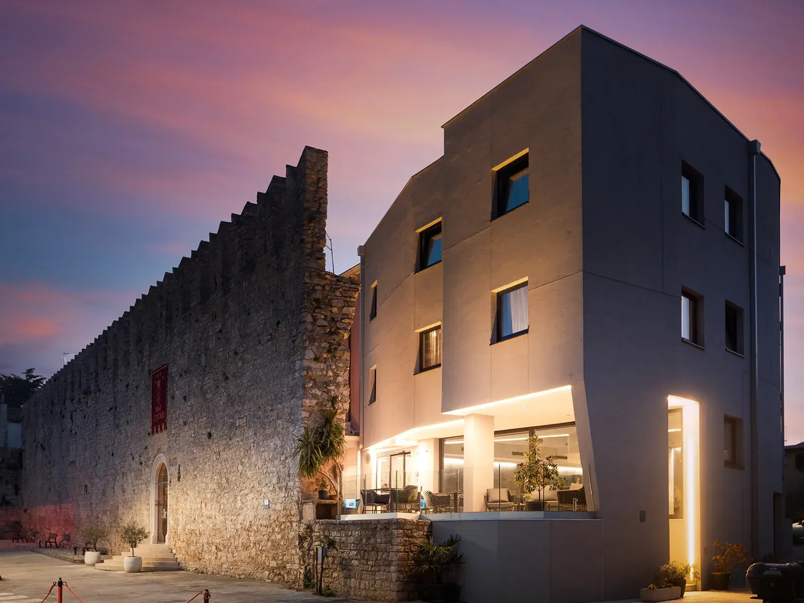 Das moderne Hotel Cittar in Novigrad, architektonisch in die historische Stadtmauer integriert, bei Dämmerung beleuchtet.