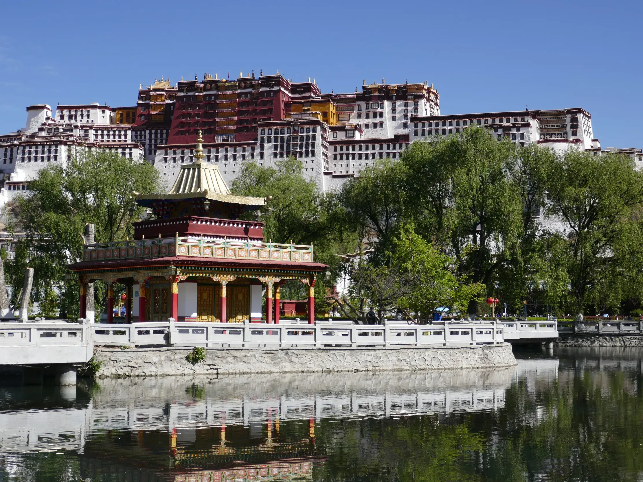 Majestätischer Potala-Palast in Lhasa, Tibet, mit einem Pavillon im Vordergrund, der sich im Wasser eines Sees spiegelt.