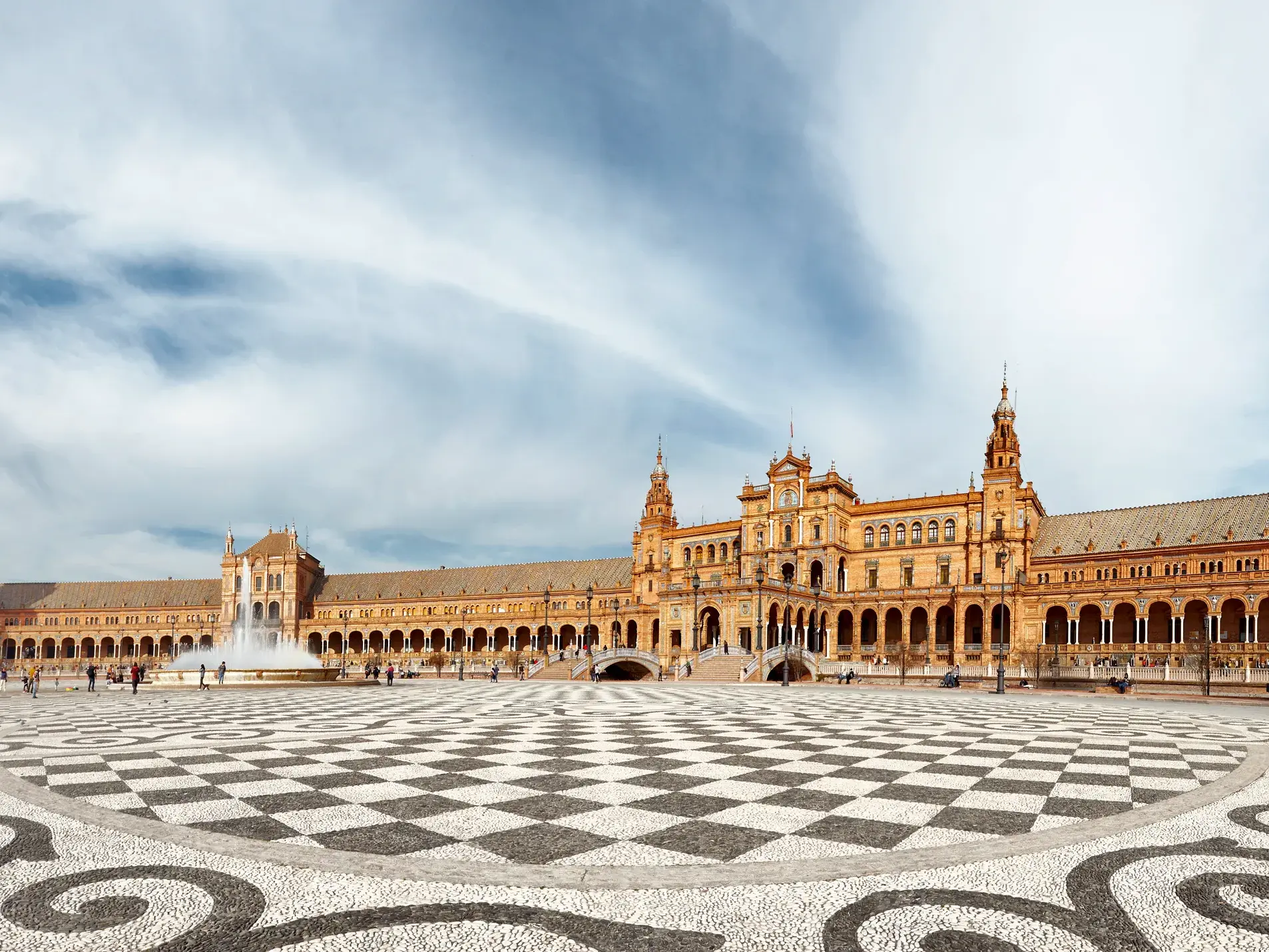 Weitläufiger, gemusterter Vorplatz des Plaza de España in Sevilla, im Hintergrund der prunkvolle Palast unter wolkigem Himmel.