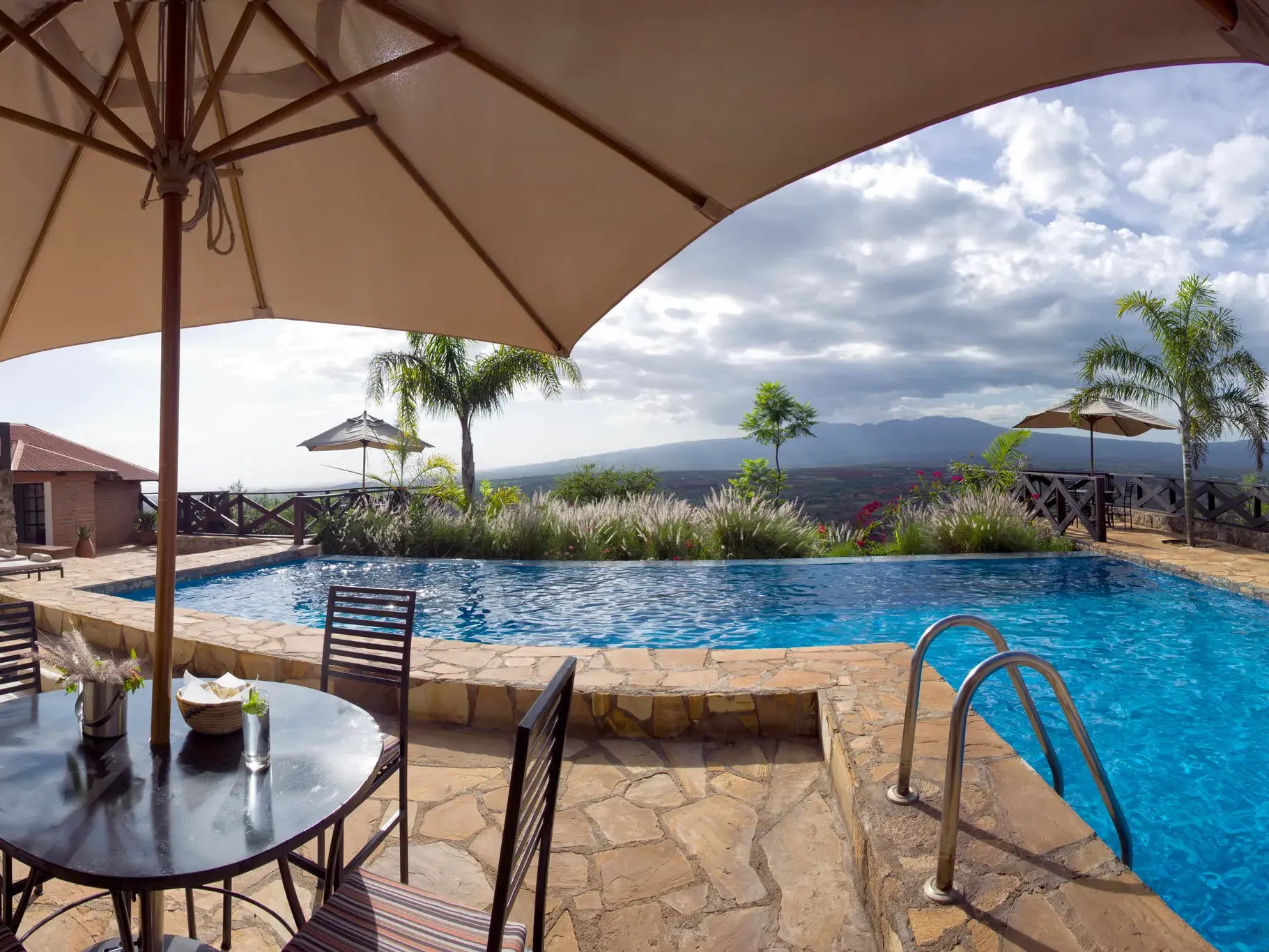 Sonnenschirm am Pool der Bashay Rift Lodge mit Panoramablick auf die weite Berglandschaft bei Karatu in Tansania.