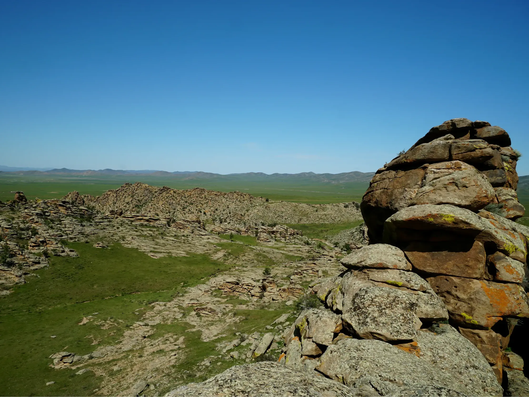 Blick von einer Anhöhe auf riesige Felsformationen in der endlosen grünen Steppenlandschaft der Mongolei bei Zorgol Khairhan.