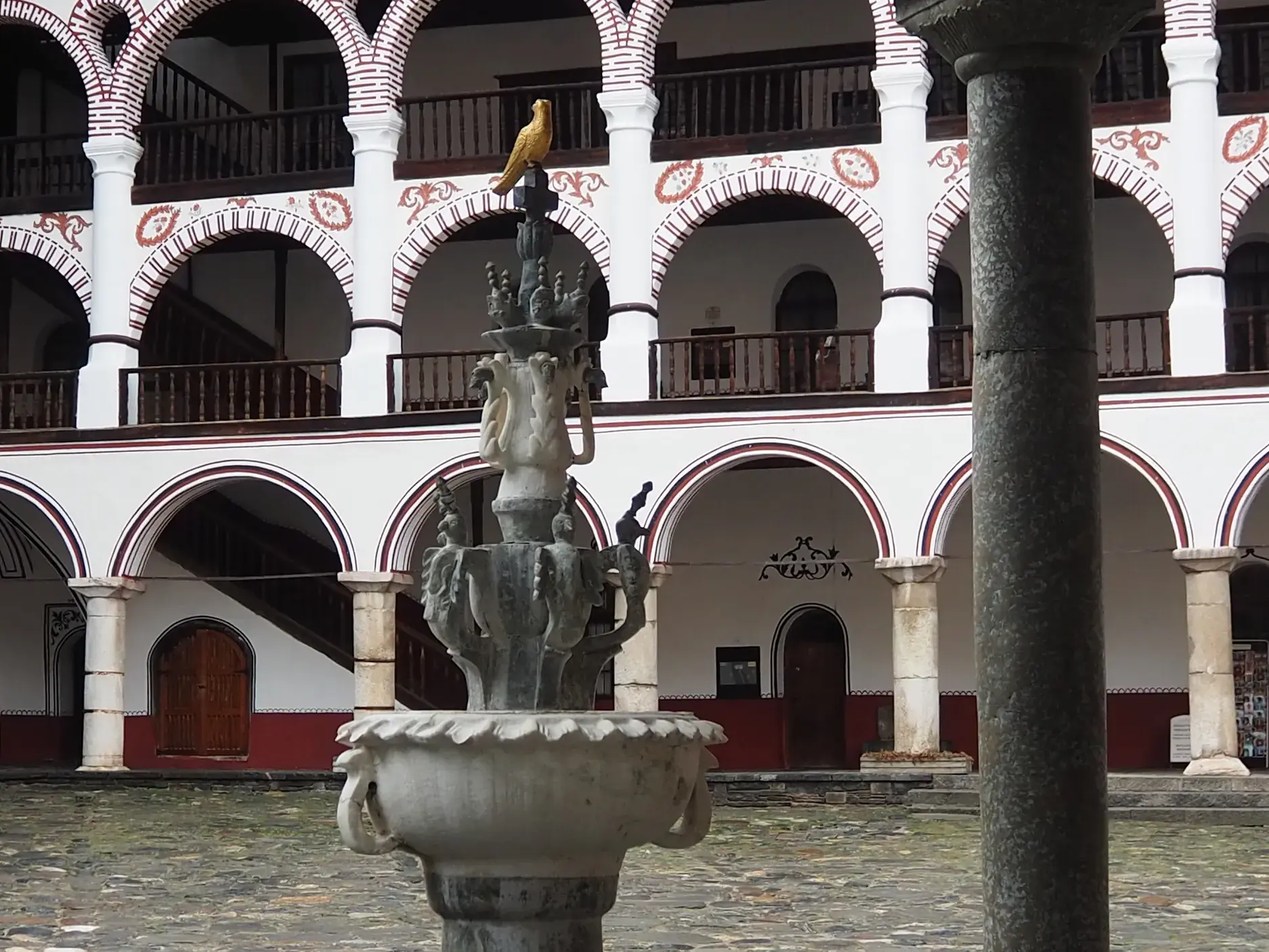 Steinerner Brunnen im Innenhof des Rila-Klosters, UNESCO-Welterbe, umgeben von kunstvoll verzierten Arkadengängen.