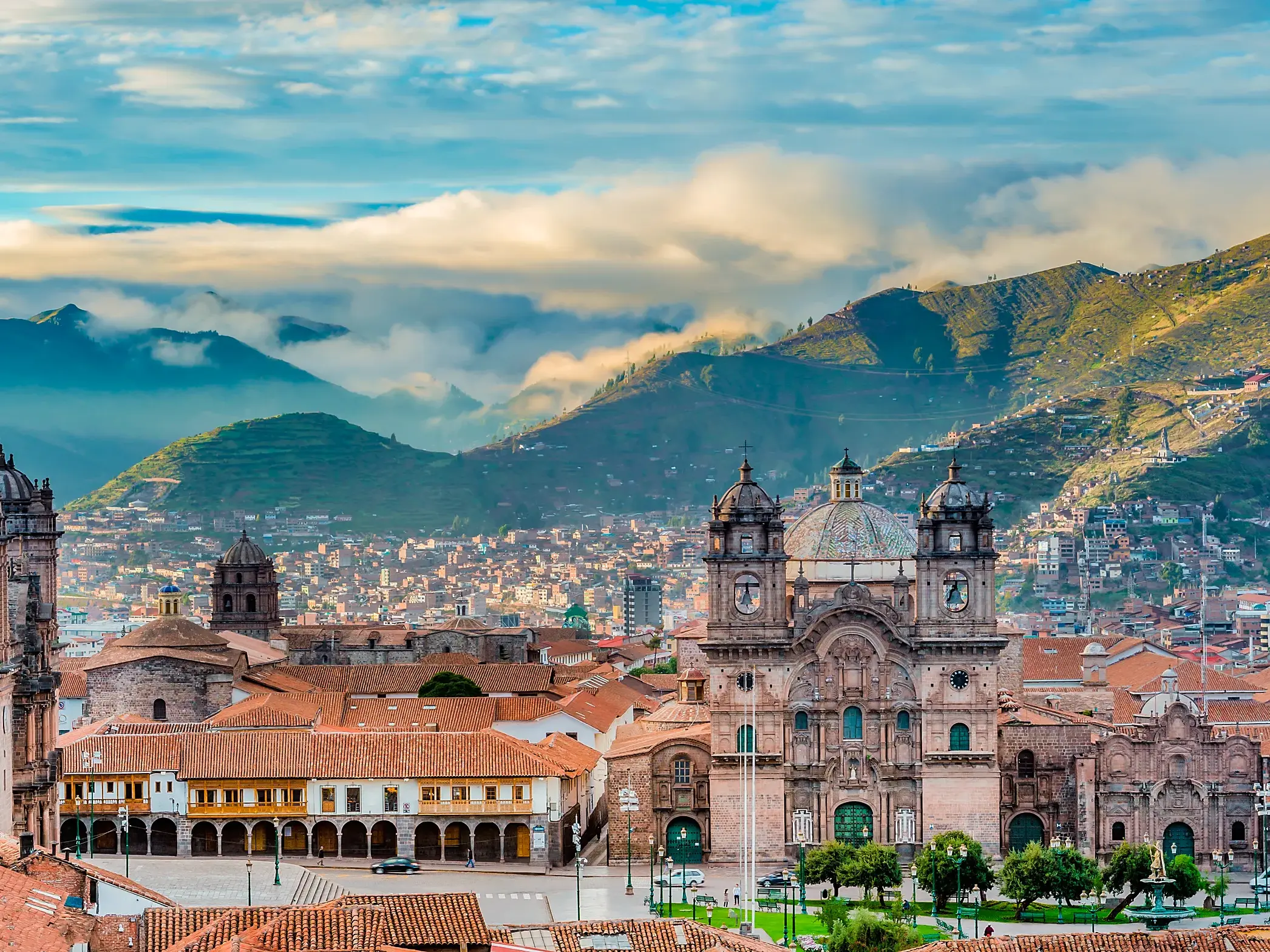 Weitblick über die roten Dächer von Cusco auf die Kathedrale und die Jesuitenkirche an der Plaza de Armas, im Hintergrund die grünen Anden.