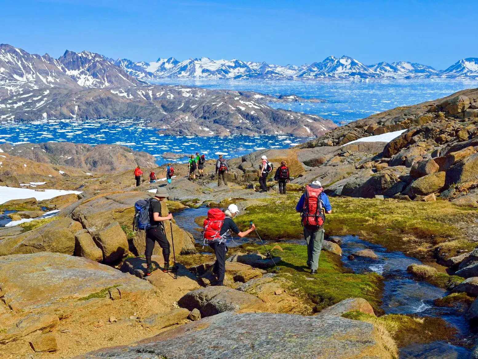 Eine Hauser-Trekkinggruppe wandert durch die felsige Landschaft Ostgrönlands mit Blick auf den Polarstrom voller Eisberge.