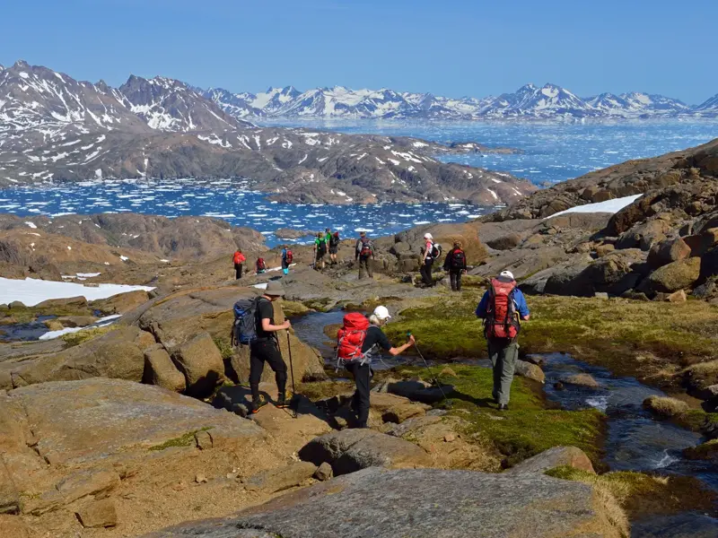Eine Hauser-Wandergruppe beim Trekking durch die arktische Landschaft Ostgrönlands mit Blick auf den eisgefüllten Polarstrom.