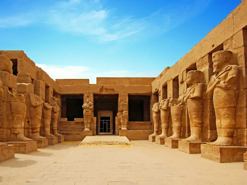 Reihen von kolossalen Pharaonenstatuen in einem Innenhof des weitläufigen Karnak-Tempels in Luxor bei strahlendem Sonnenschein.
