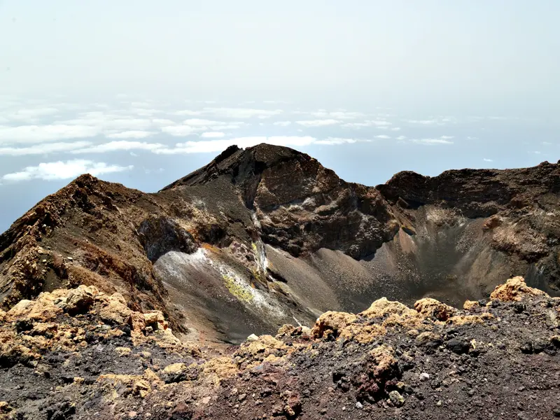 Eindrucksvoller Blick in den dunklen, zerklüfteten Krater des Vulkans Pico do Fogo auf den Kapverden über einem Wolkenmeer.