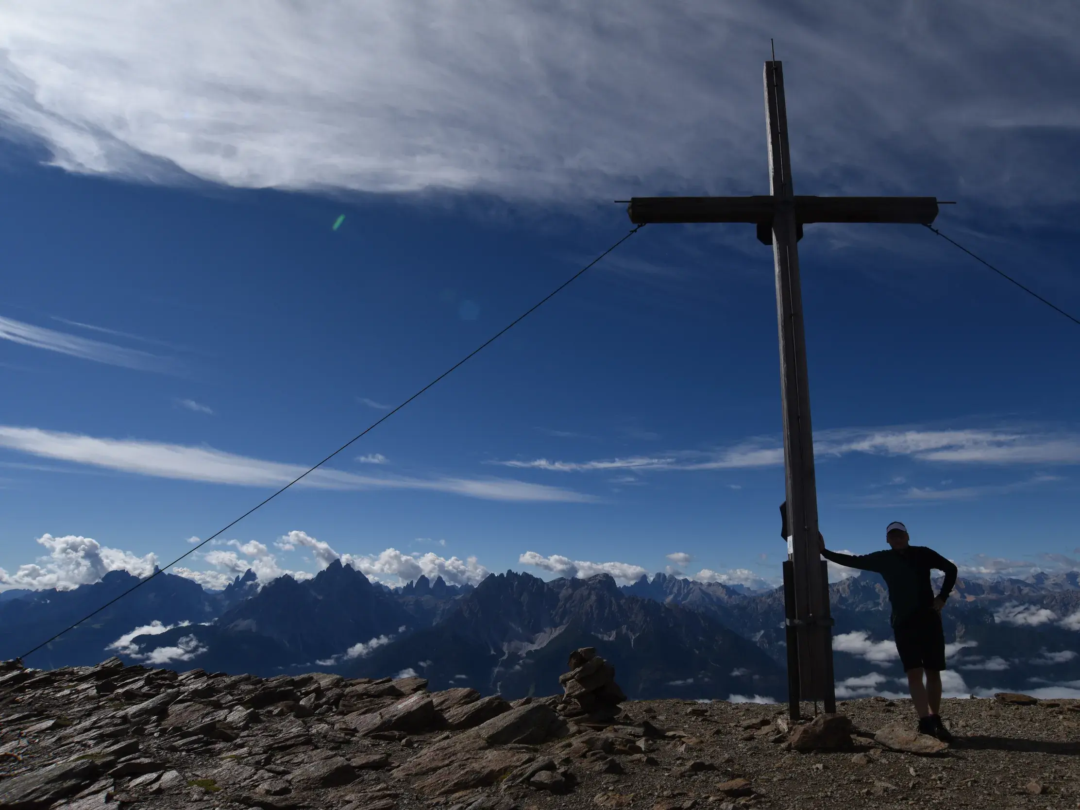 Ein Wanderer steht nach dem Aufstieg stolz am Gipfelkreuz des Toblacher Pfannhorns mit Panoramablick auf die Dolomiten.