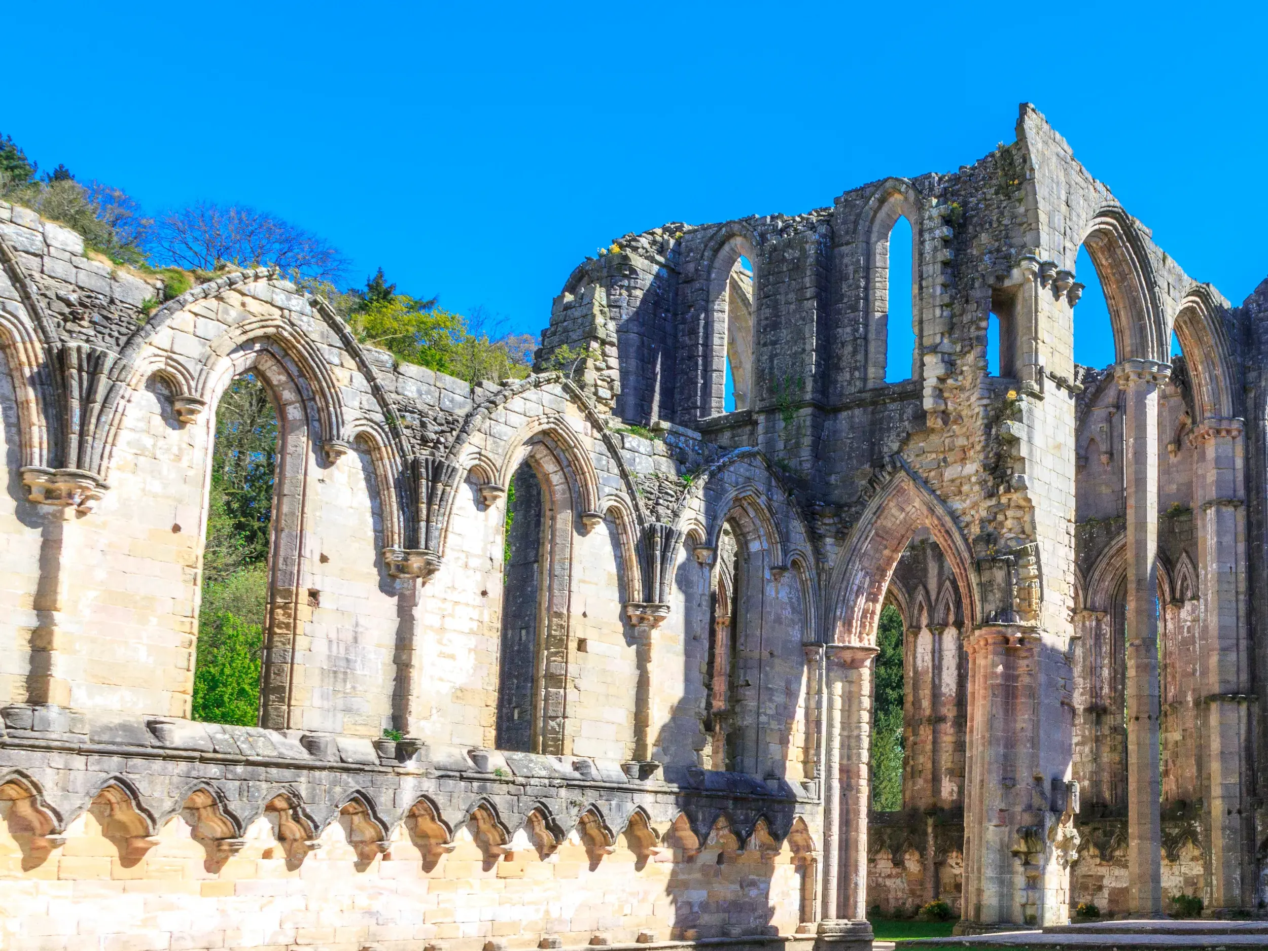 Gotische Steinbögen der Ruinen der Zisterzienserabtei Fountains Abbey, UNESCO-Welterbe, unter blauem Himmel in England.