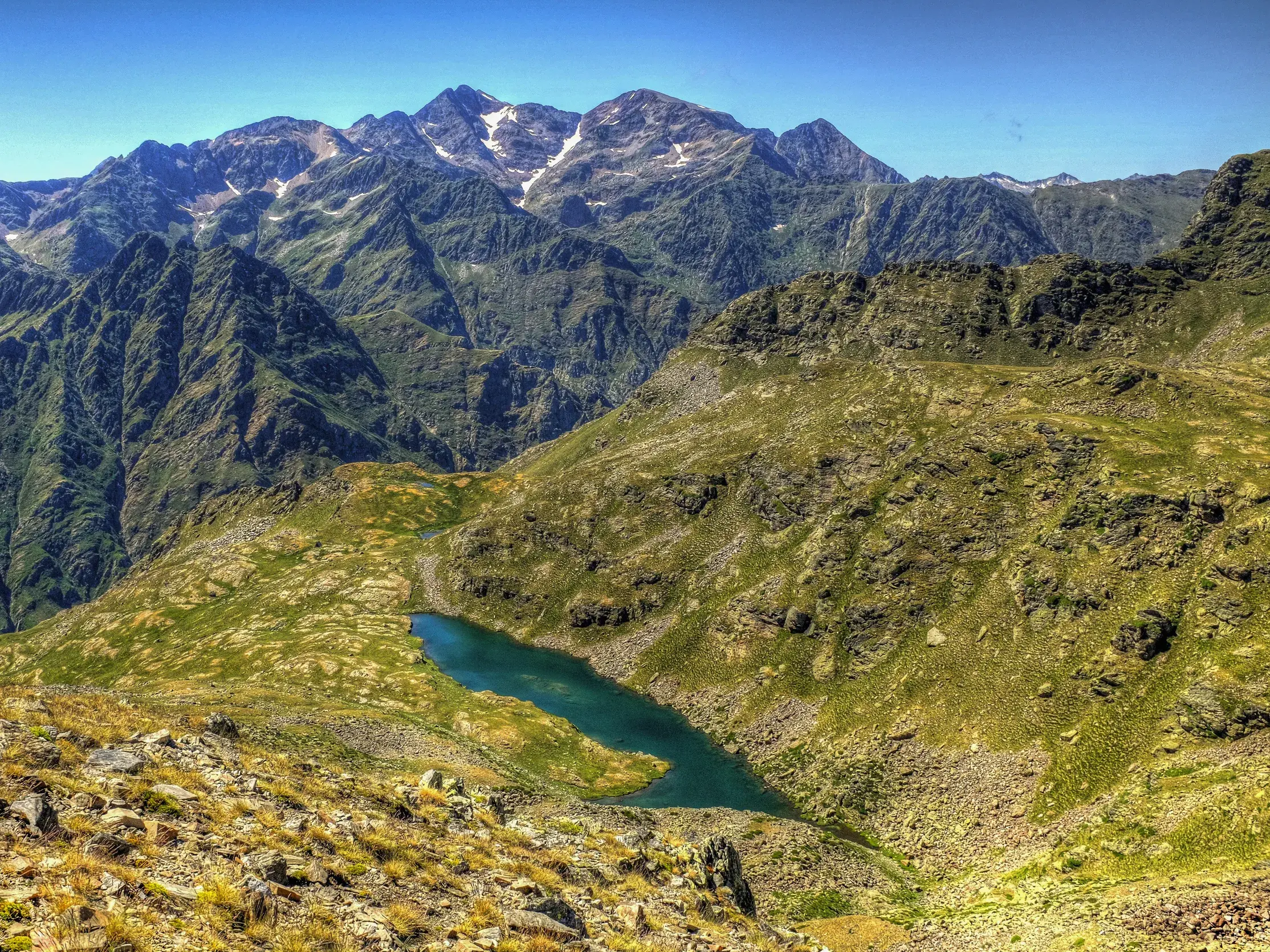 Ausblick beim Wandern in Andorra: ein blauer Karsee in einem Hochgebirgstal vor der Kulisse der schroffen Pyrenäen-Gipfel.