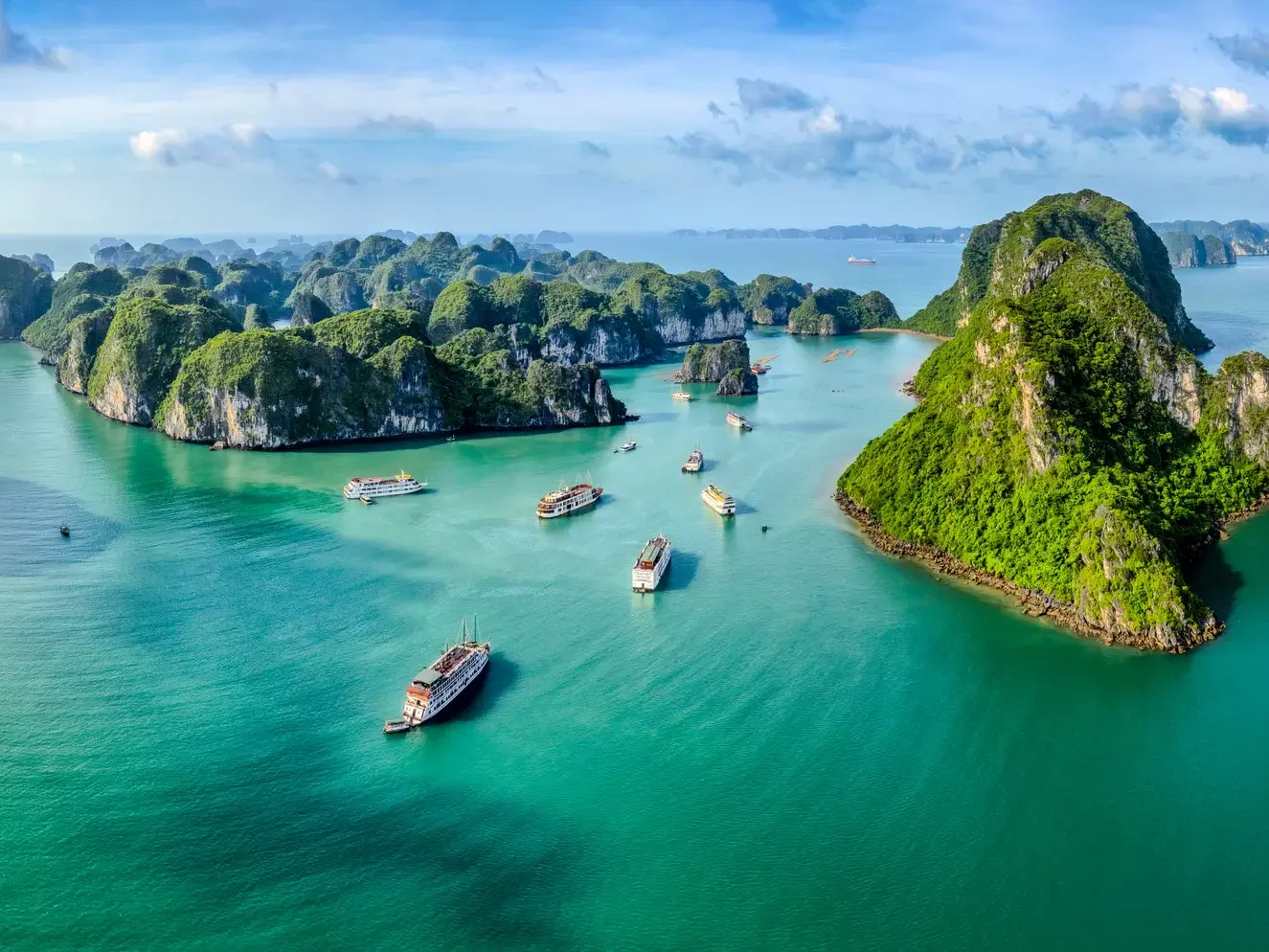 Spektakuläre Luftaufnahme von traditionellen Dschunken auf dem smaragdgrünen Wasser der Halongbucht in Vietnam.
