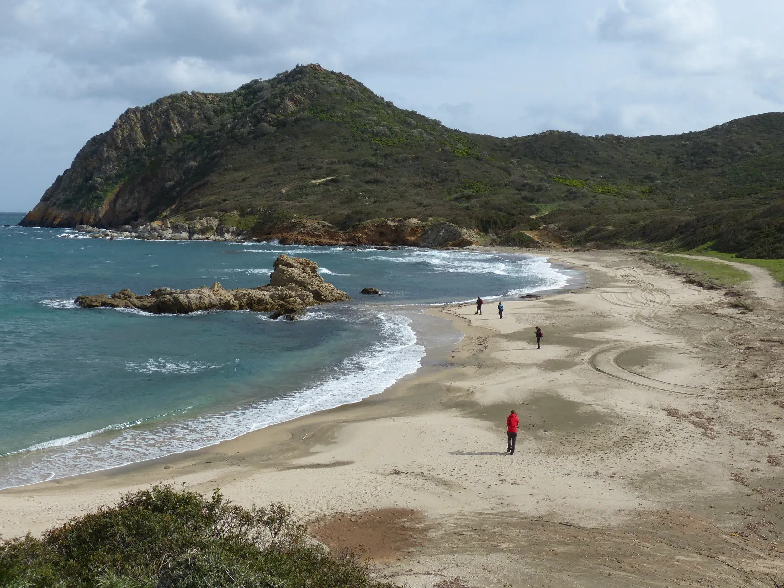 Eine kleine Wandergruppe erkundet den weiten Sandstrand während einer Küstenwanderung am Capo Pecora auf Sardinien.
