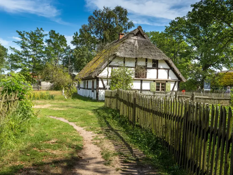 Traditioneller Bauernhof der Slowinzen im Freilichtmuseum Kluki, ein Fachwerkhaus mit Reetdach und rustikalem Holzzaun.