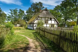Traditioneller Bauernhof der Slowinzen im Freilichtmuseum Kluki, ein Fachwerkhaus mit Reetdach und rustikalem Holzzaun.