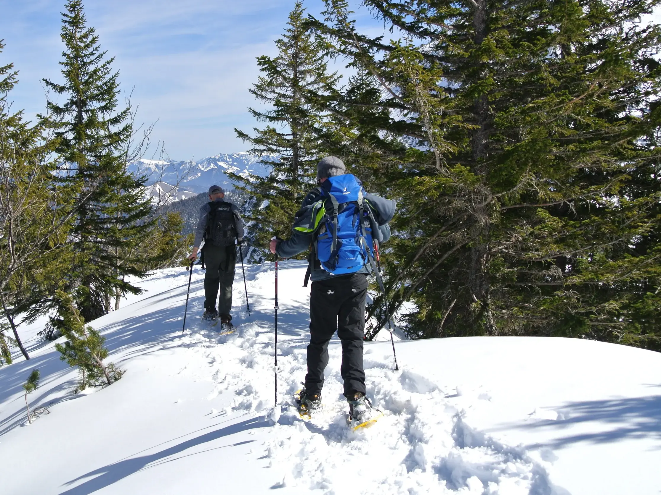 Zwei Personen bei einer Schneeschuhwanderung auf einem verschneiten Grat im Naturpark Karwendel mit Blick auf die Berge.
