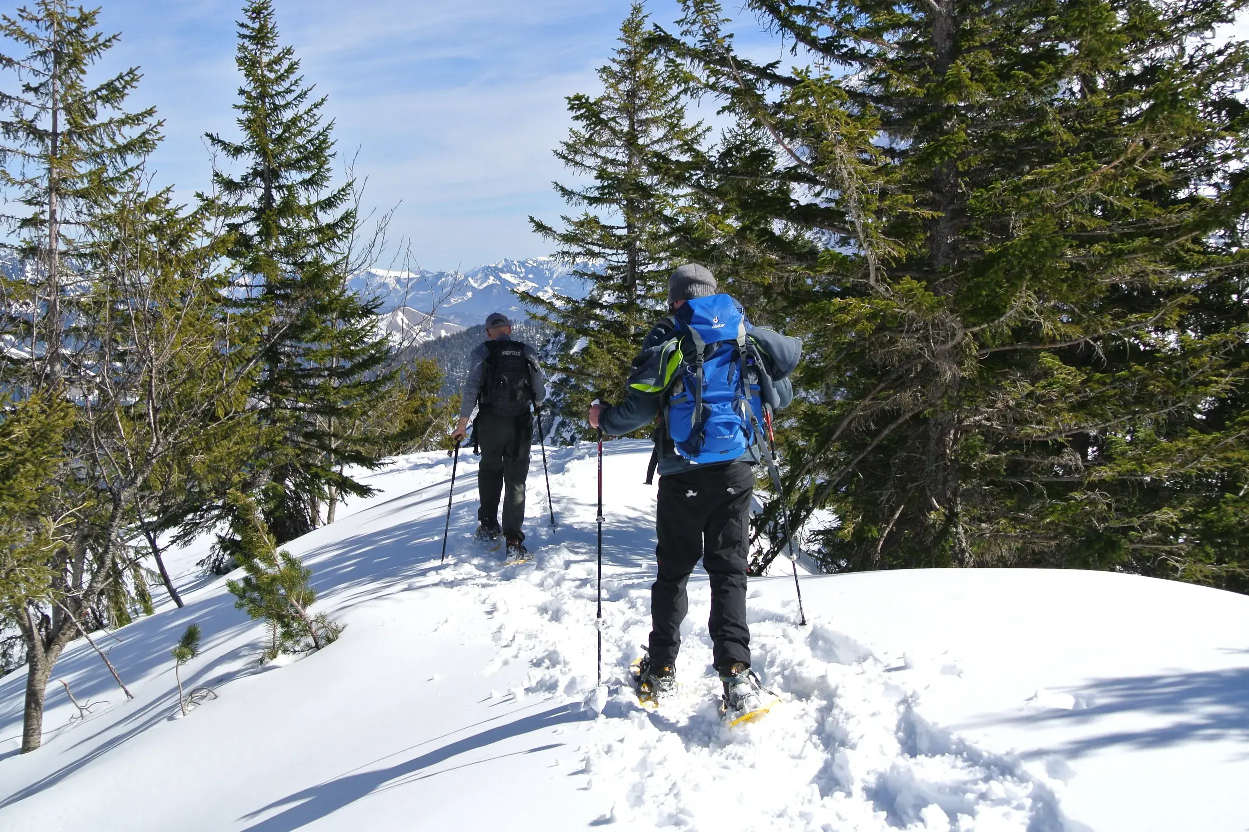 Zwei Personen bei einer Schneeschuhwanderung auf einem verschneiten Grat im Naturpark Karwendel mit Blick auf die Berge.