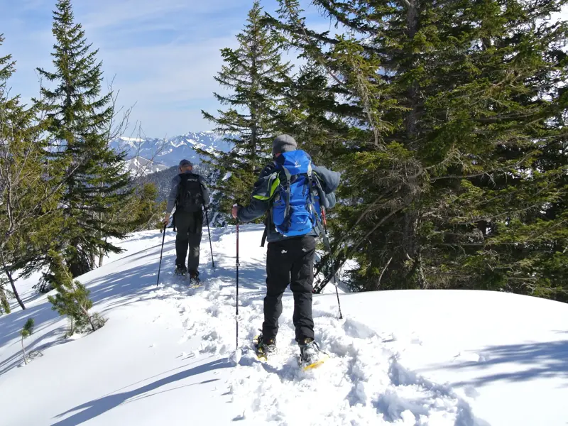 Zwei Personen bei einer Schneeschuhwanderung auf einem verschneiten Grat im Naturpark Karwendel mit Blick auf die Berge.