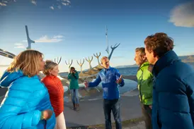 Ein Studiosus-Reiseleiter erklärt seiner Reisegruppe eine moderne Wikingerschiff-Skulptur am sonnigen Hafen von Reykjavik.