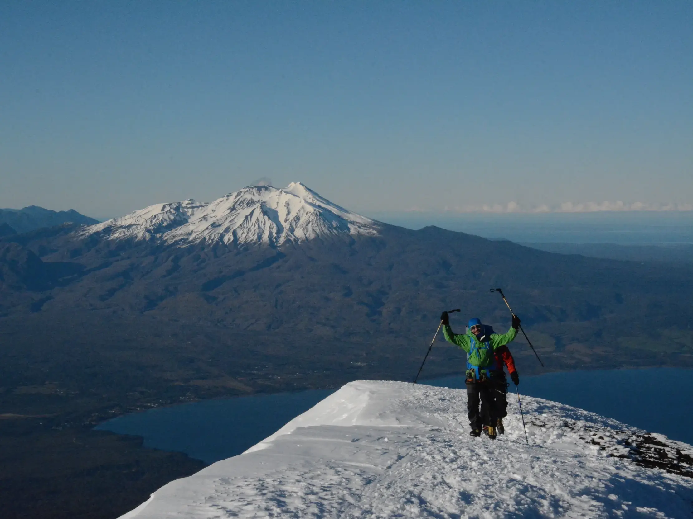 Ein Trekker jubelt auf dem schneebedeckten Gipfel des Vulkans Osorno mit Blick auf den Llanquihue-See und die Anden in Chile.