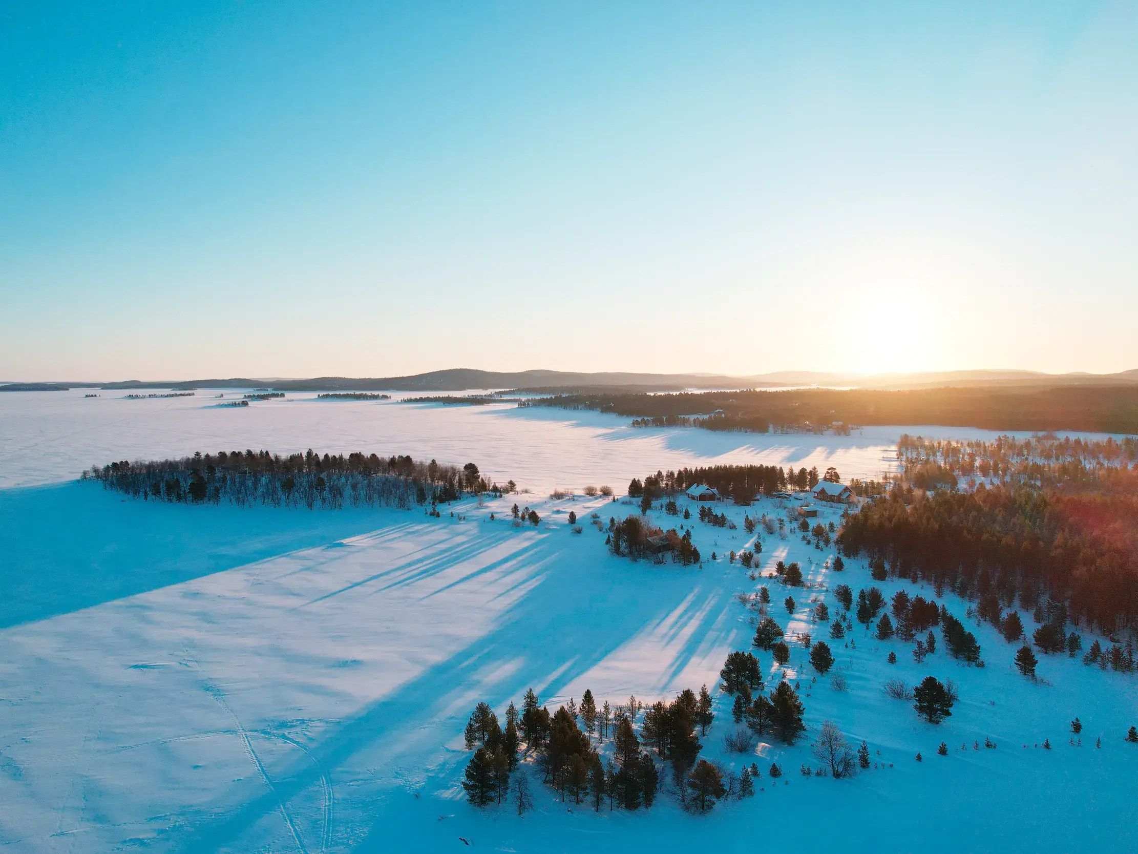 Die tiefstehende Wintersonne taucht die verschneite Fjell-Landschaft Lapplands mit ihren gefrorenen Seen in goldenes Licht.