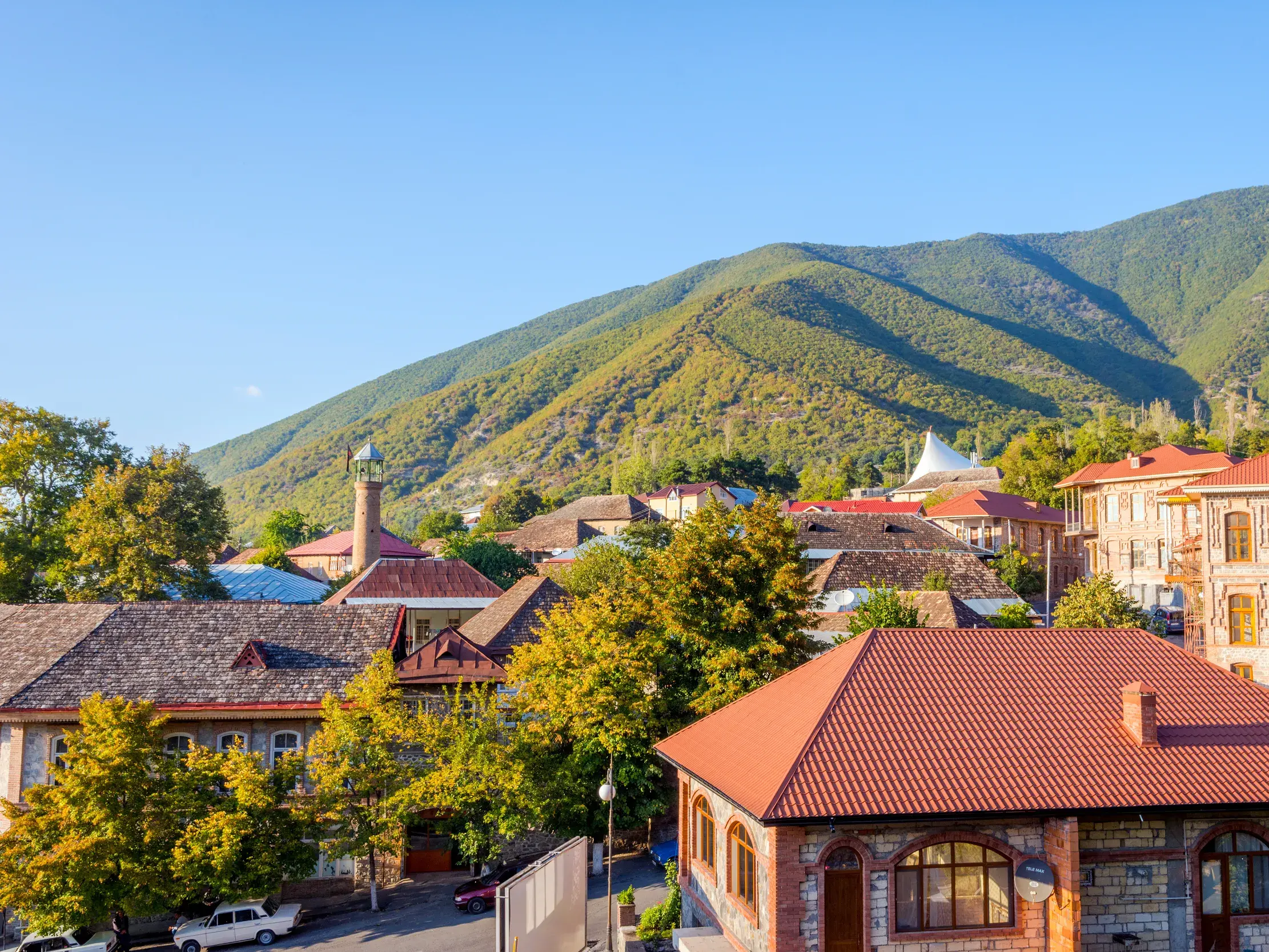 Blick über die traditionellen Häuser mit roten Dächern in Sheki, Aserbaidschan, vor der grünen Bergkulisse des Kaukasus.