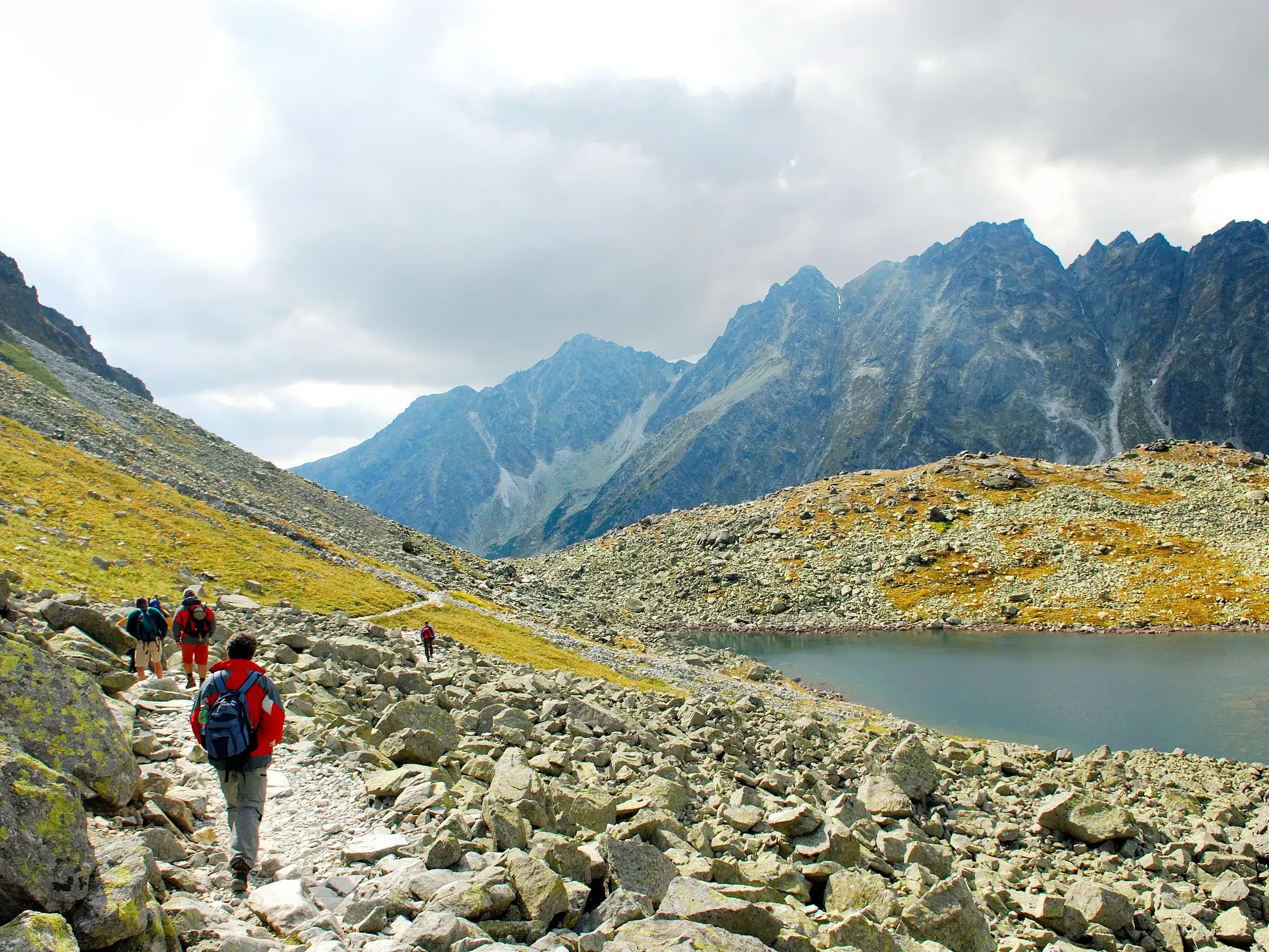 Wanderer auf einem Trekkingpfad am Ufer eines Bergsees mit Blick auf die schroffen Gipfel der Hohen Tatra.