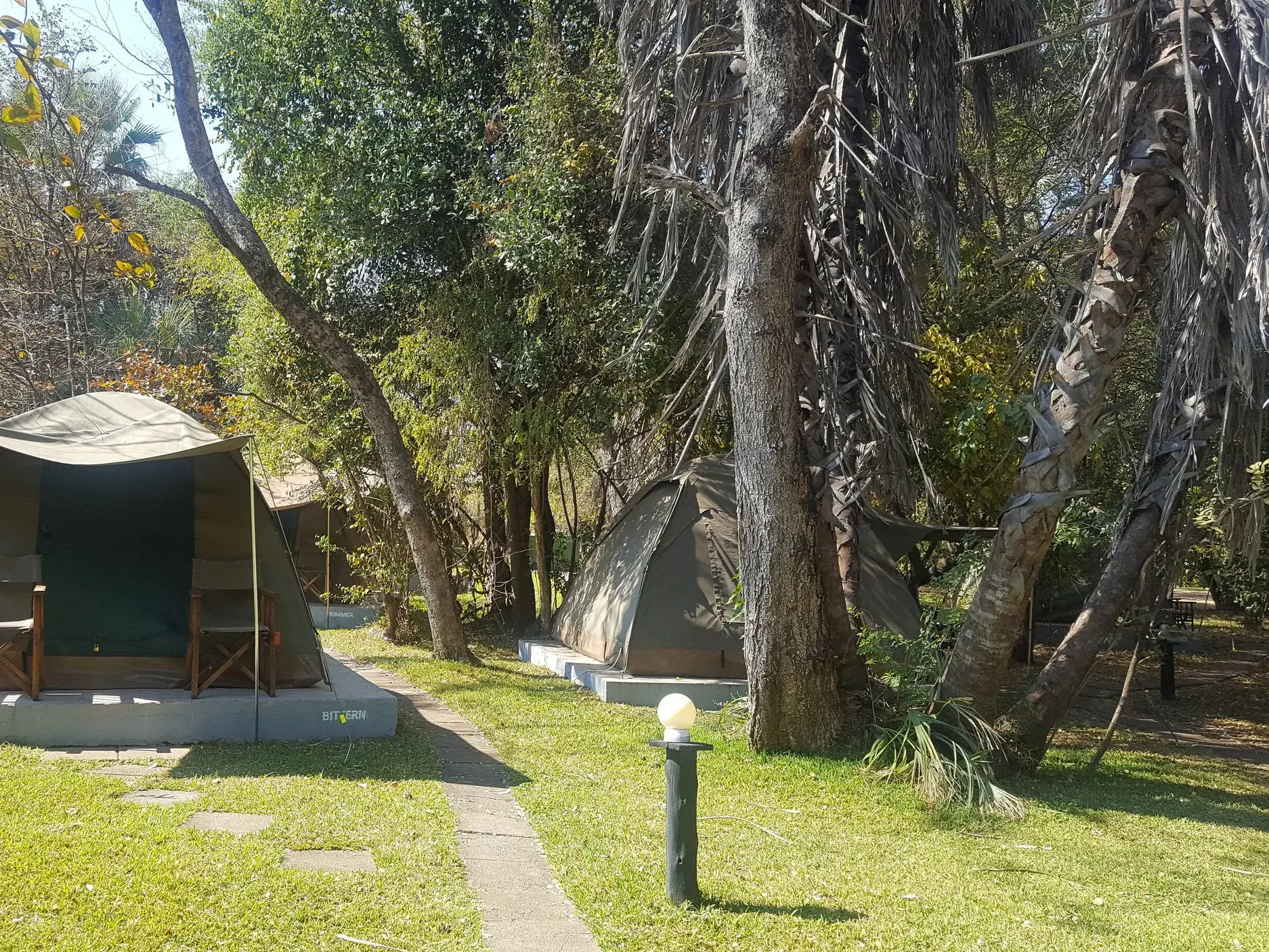 Große Safari-Zelte auf einem Campingplatz nahe der Victoriafälle in Sambia, umgeben von üppiger, grüner Vegetation.