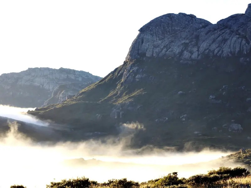 Trekking in Madagaskar: Schroffe Granitgipfel des Andringitra-Gebirges ragen bei Sonnenaufgang aus einem Nebelmeer.