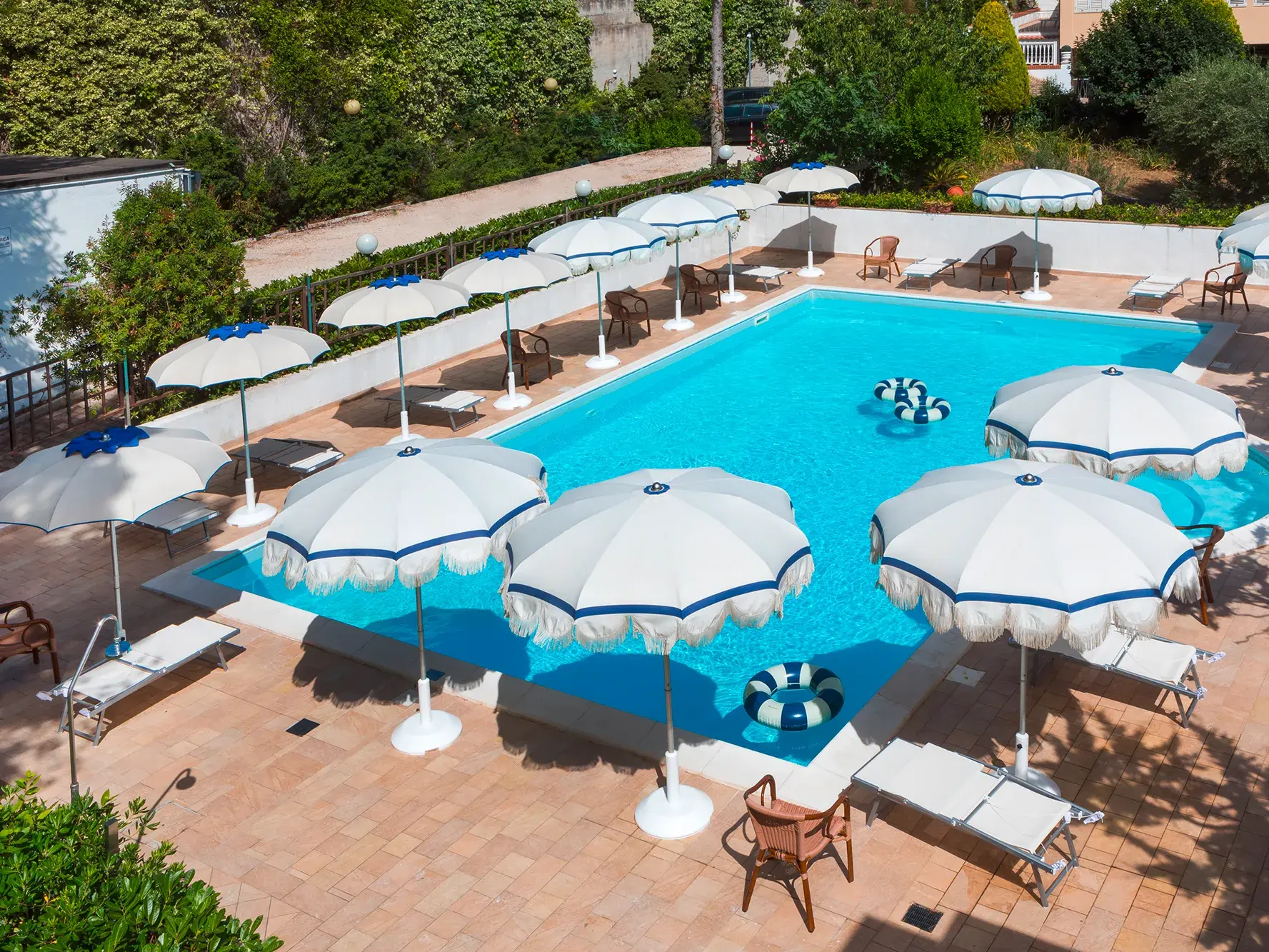 Sonnige Poolterrasse im Hotel Murè in Numana, umgeben von weißen Sonnenschirmen und Liegen am türkisblauen Wasser.