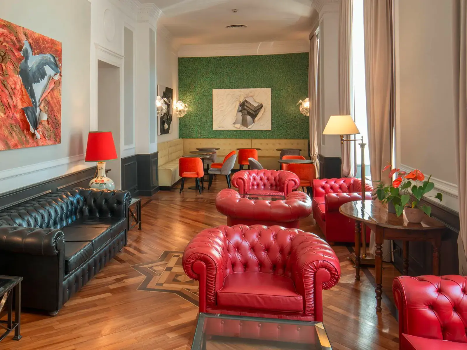Stilvolle Lounge im Hotel Nord Nuova in Rom mit roten Ledersesseln, einem schwarzen Sofa und moderner Kunst an der Wand.