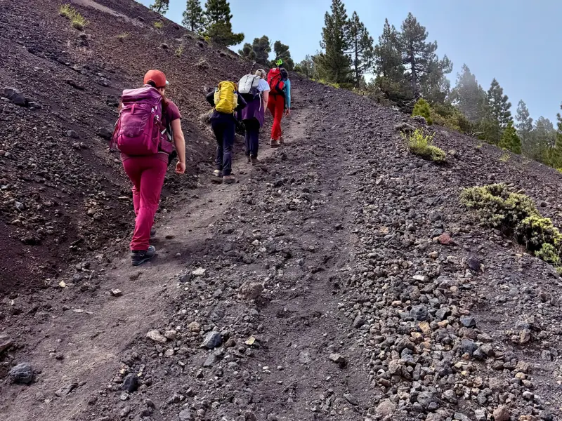 Vier Wanderer mit Rucksäcken auf einem steilen Anstieg durch die karge Vulkanlandschaft der Cumbre Vieja auf La Palma.