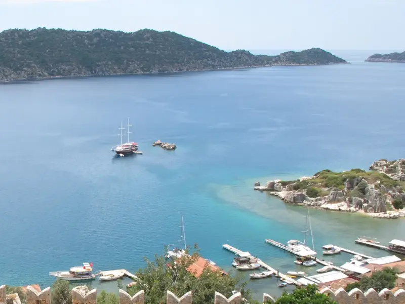 Panoramablick von der Burg Simena auf die türkisfarbene Bucht von Üçağız mit Booten und der lykischen Küste im Hintergrund.