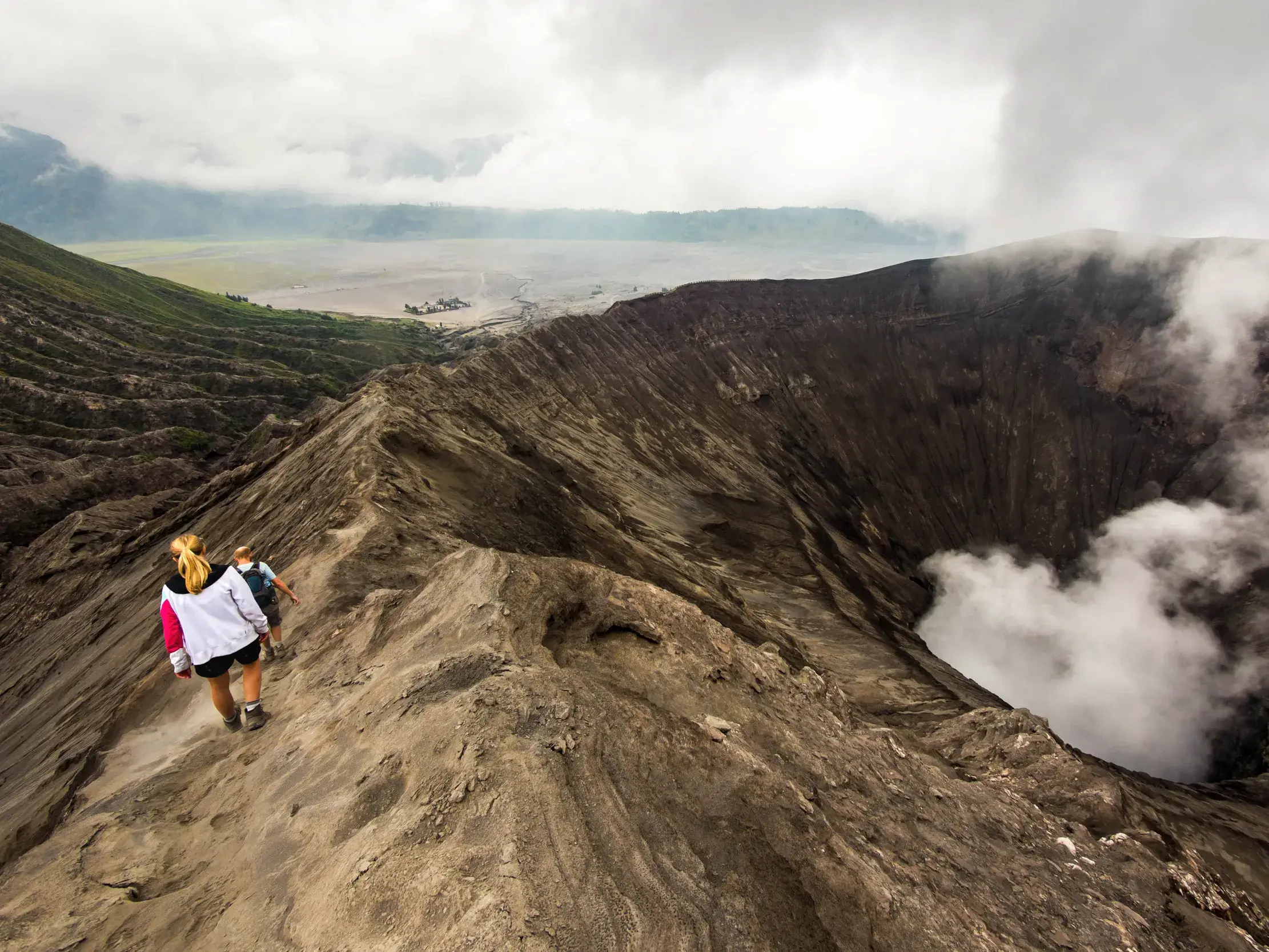 Zwei Wanderer auf einem schmalen Pfad am Kraterrand des rauchenden Vulkans Gunung Bromo auf der Insel Java.