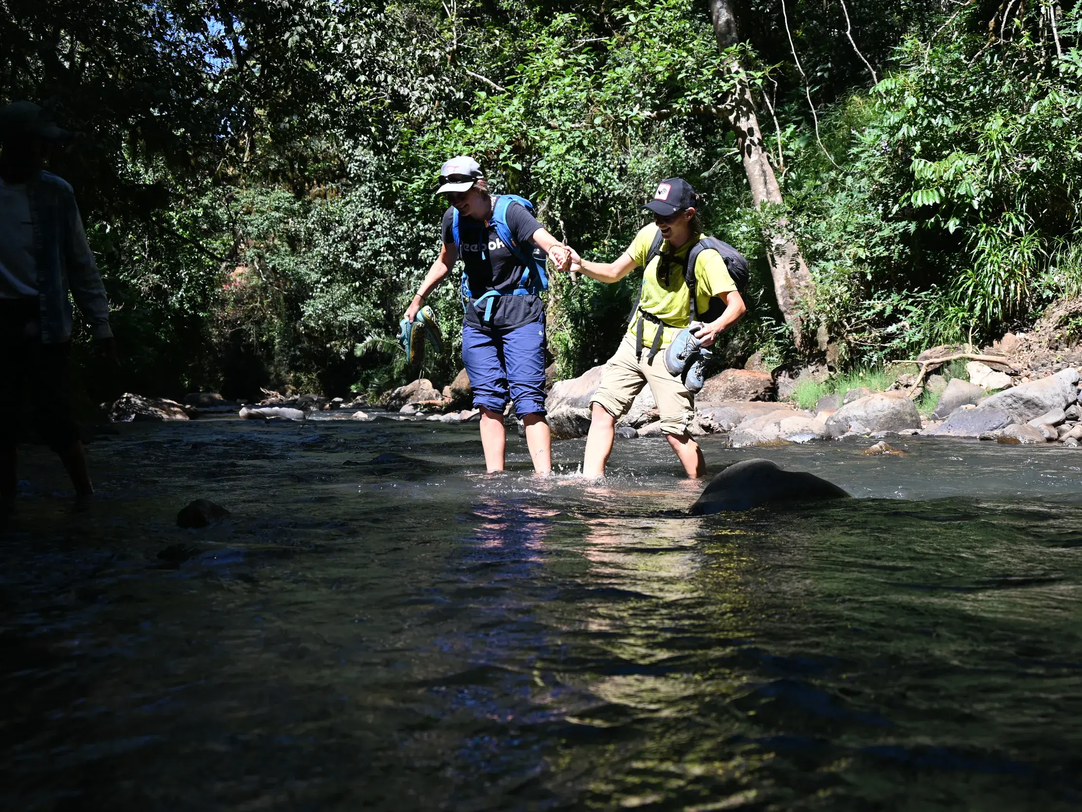 Zwei Wanderer einer Hauser Reisegruppe durchqueren Hand in Hand einen Fluss beim Trekking im grünen Gurage-Gebiet in Äthiopien.