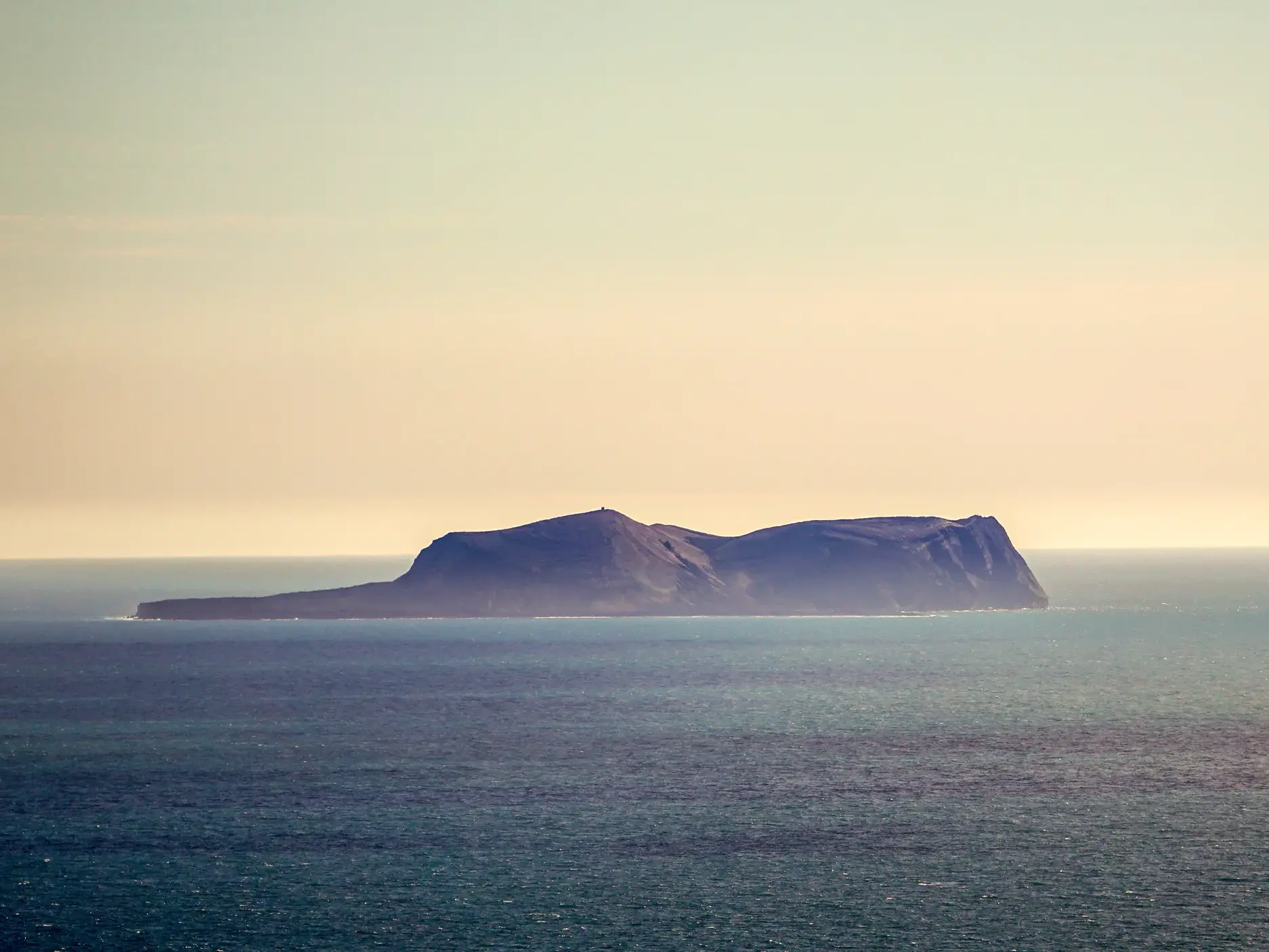 Eine der einsamen Westmännerinseln erhebt sich bei sanftem Licht aus dem weiten Nordatlantik vor der Küste Islands.