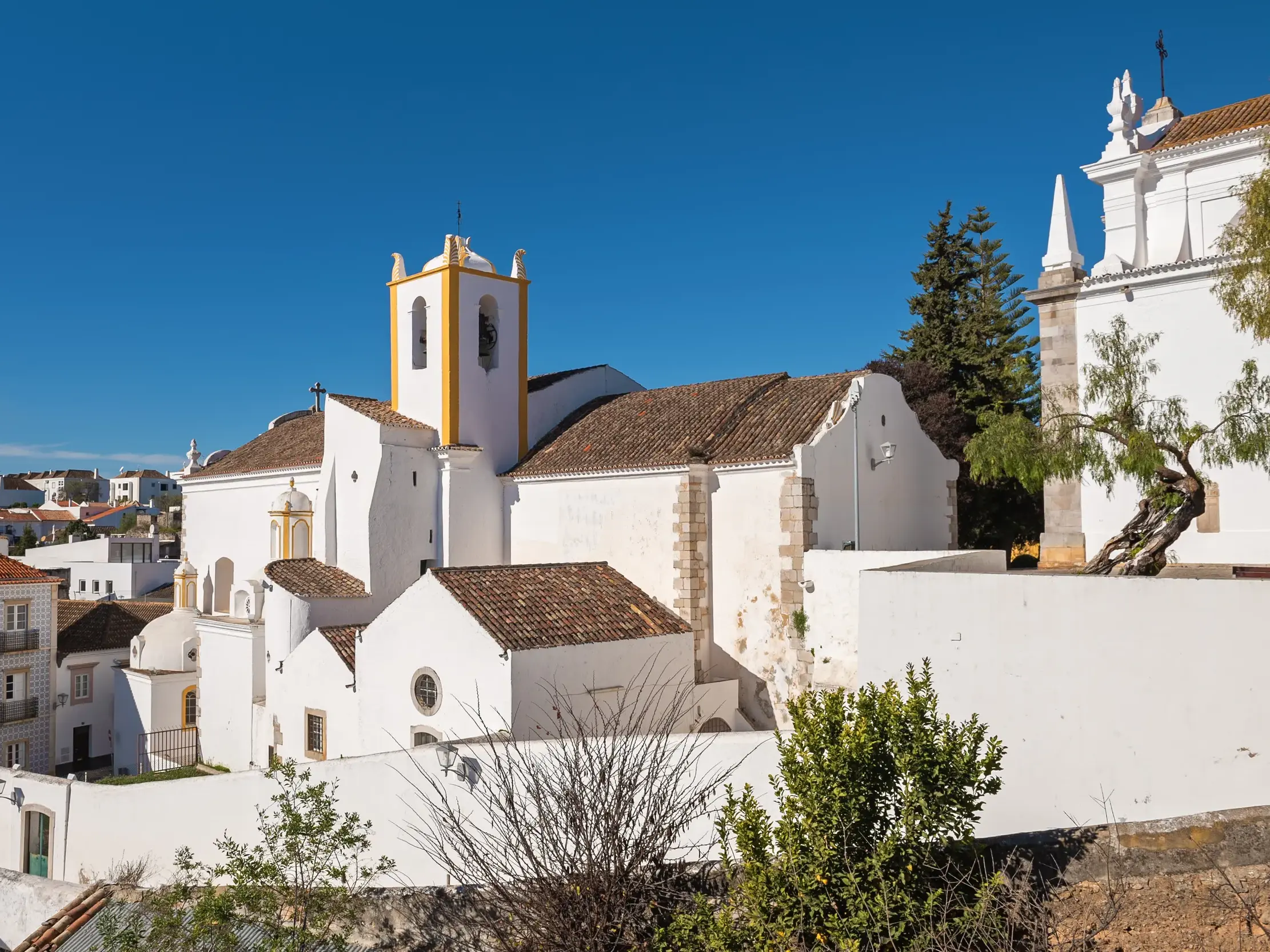 Die weißen Häuser und die Kirche der mittelalterlichen Altstadt von Tavira an einem sonnigen Tag an der Algarve.