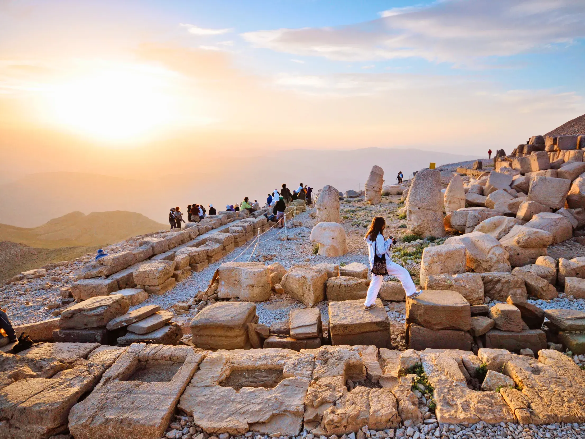 Eine Reisende erkundet die antiken Steinterrassen und Monumentalköpfe auf dem Gipfel des Nemrut Dag bei Sonnenuntergang.