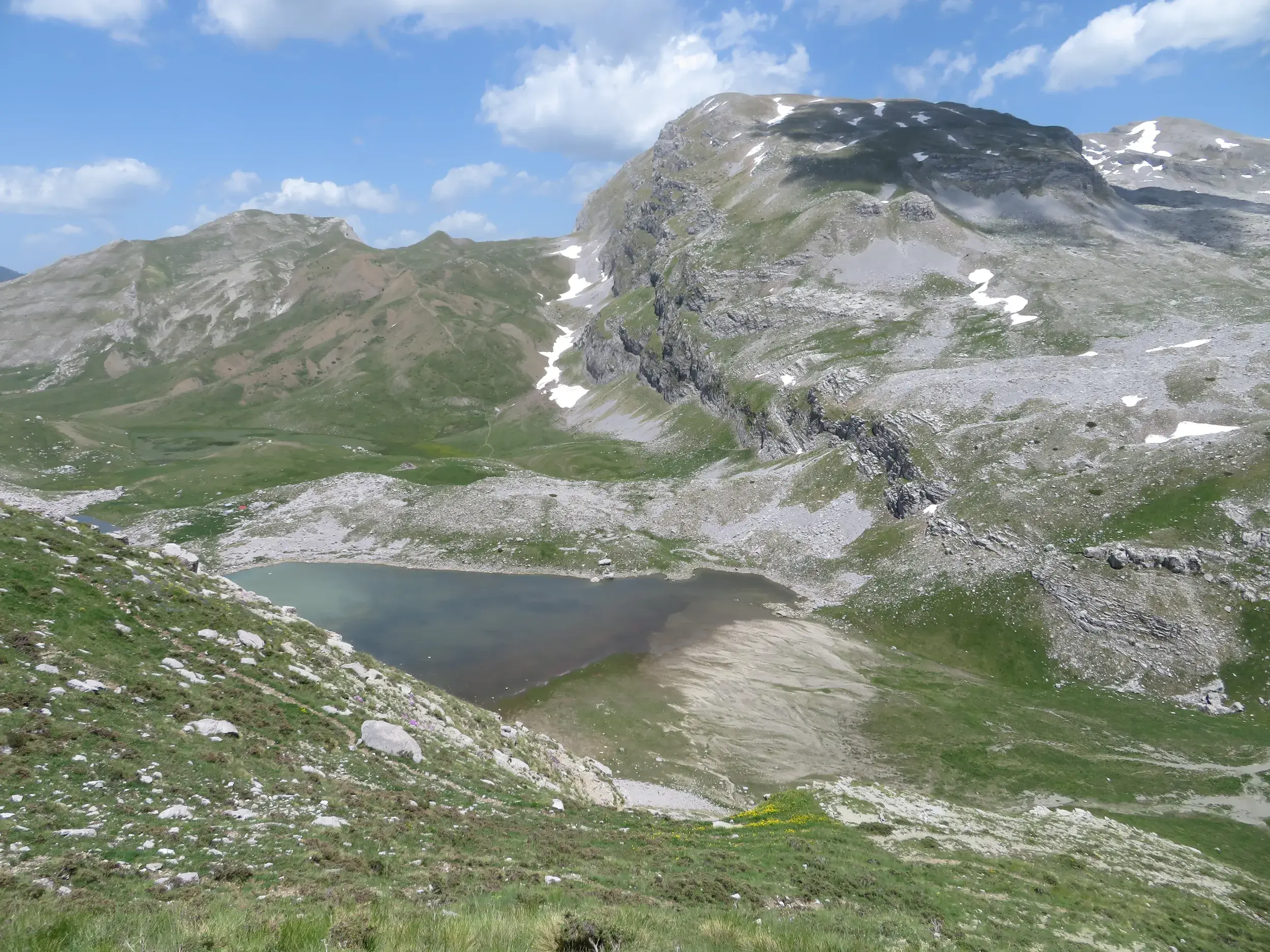 Blick von einem grasbewachsenen Hang auf den sagenumwobenen Drachensee Drakolimni in der Bergwelt der Zagori-Region.