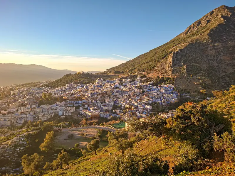 Panoramablick von einer Wanderung im Rif-Gebirge auf die blau-weiße Medina von Chefchaouen bei Sonnenaufgang.