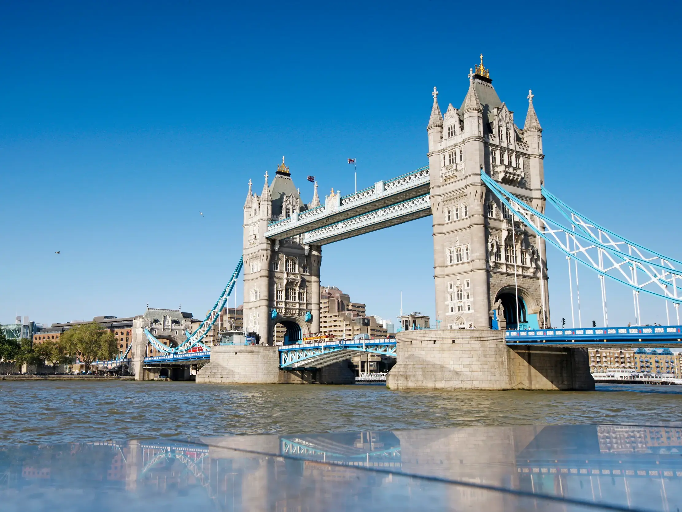Blick vom Wasser der Themse auf die neugotische Tower Bridge in London unter strahlend blauem Himmel.