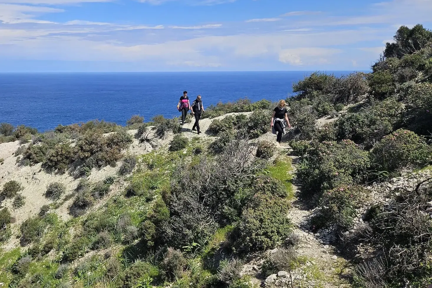 Eine kleine Wandergruppe auf dem Beşparmak-Trail an der Küste Nordzyperns, mit weitem Ausblick auf das tiefblaue Mittelmeer.