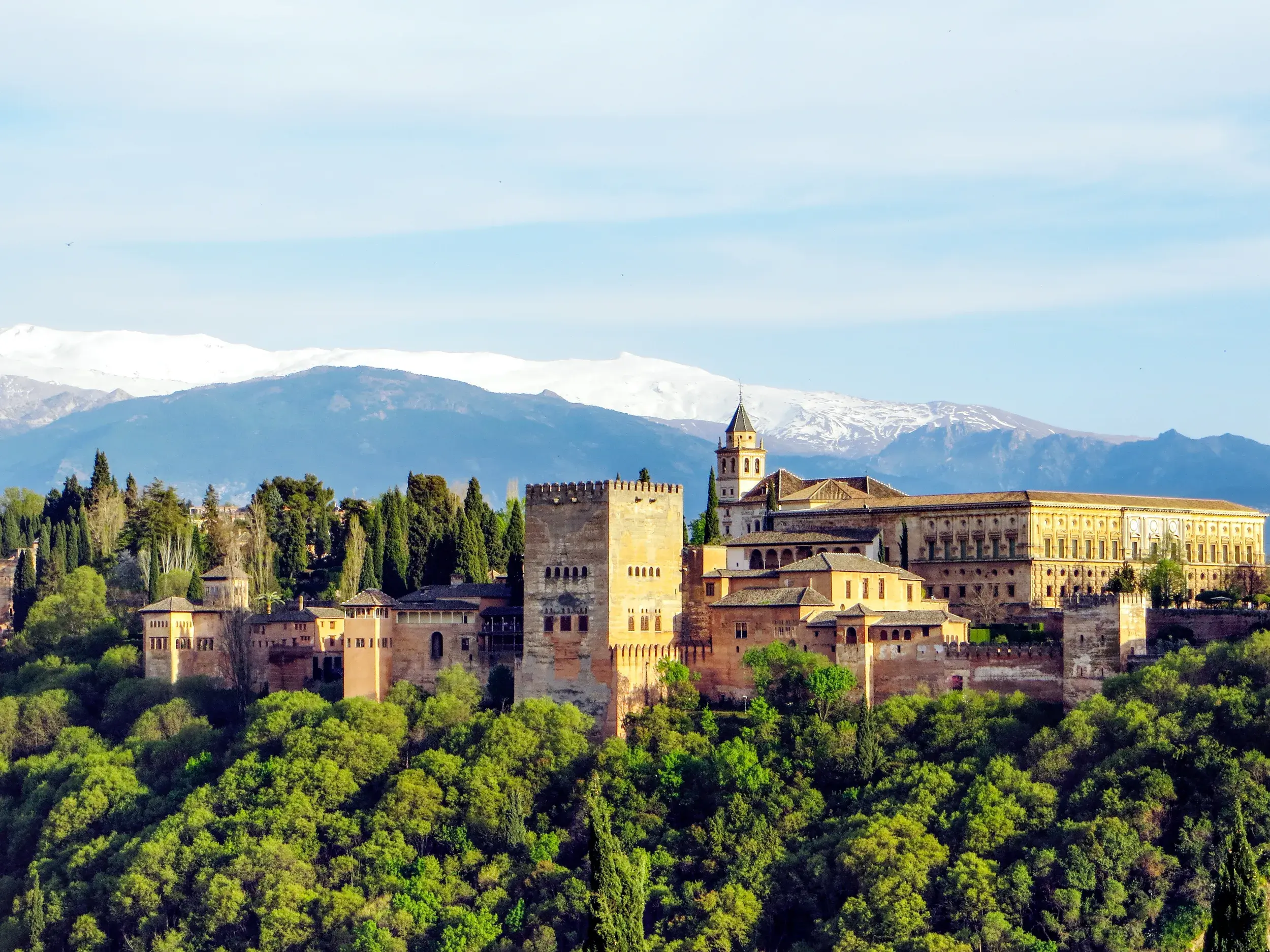 Die historische Alhambra thront auf einem bewaldeten Hügel in Granada vor den schneebedeckten Gipfeln der Sierra Nevada.