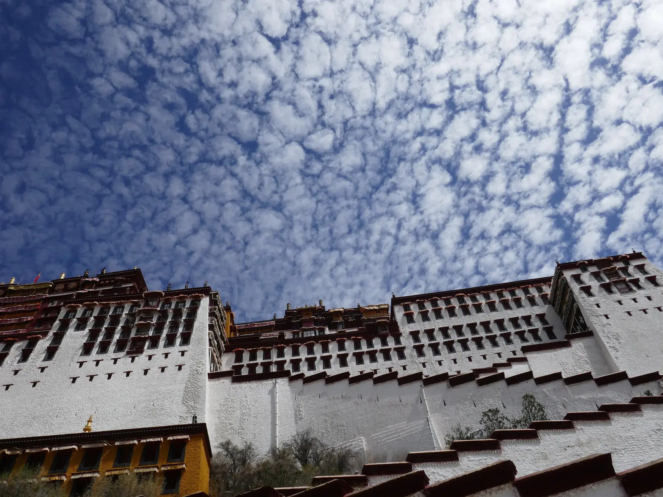 Imposante, weiße Fassade des Potala-Palastes in Lhasa, Tibet, fotografiert von unten gegen den dramatischen Wolkenhimmel.
